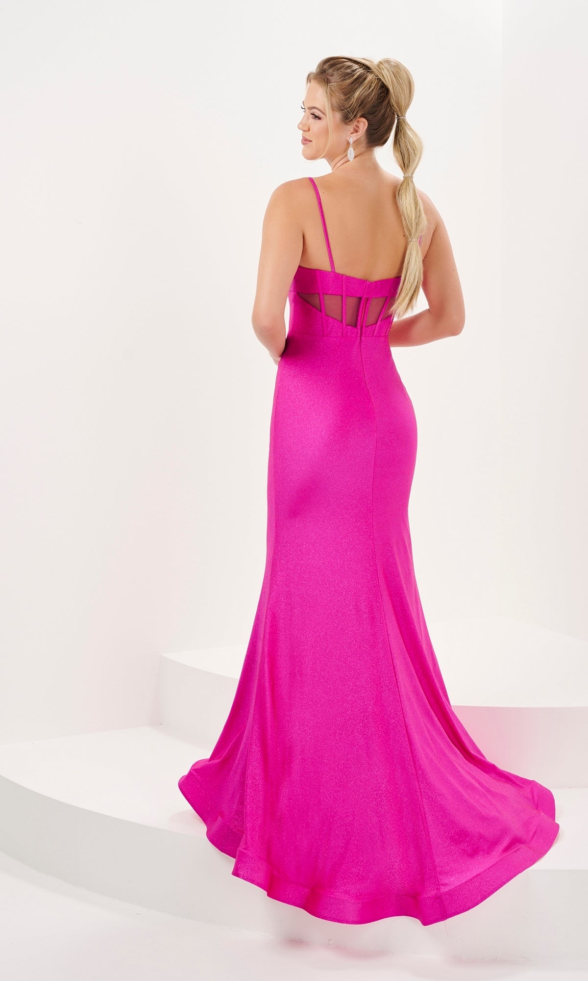 A woman stands on white steps facing away, wearing the Long Prom Dress 16062 by Tiffany—a bright pink, floor-length glitter formal gown with thin straps and sheer panel detailing.